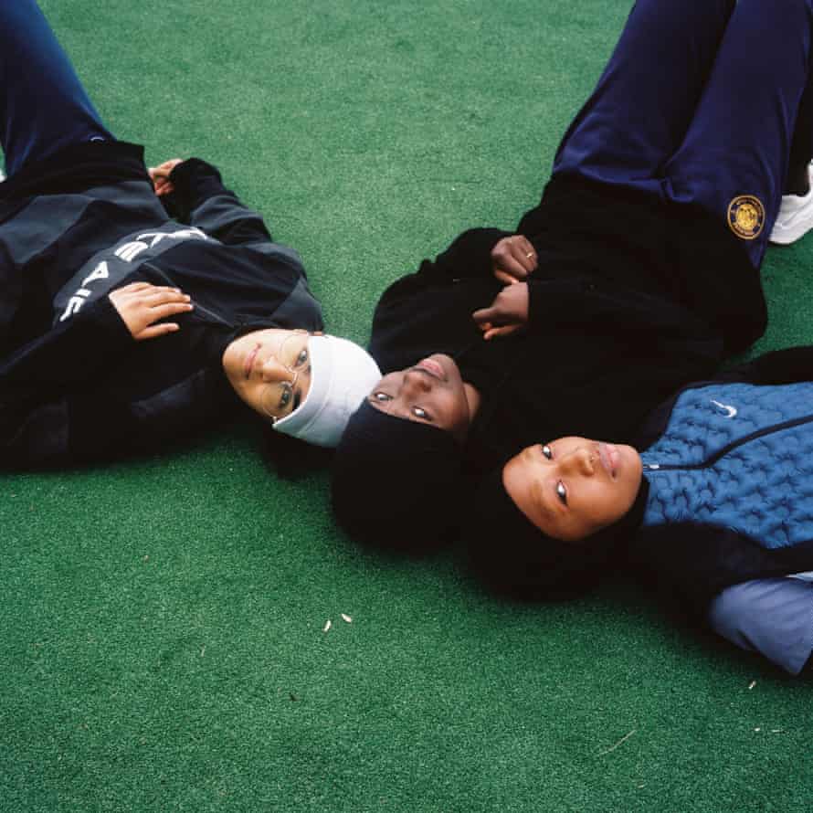Les Hijabeuses (de gauche à droite) : Zamya, Diawara et Doucouré sont allongés têtes ensemble au sol sur le terrain de football de Montreuil.