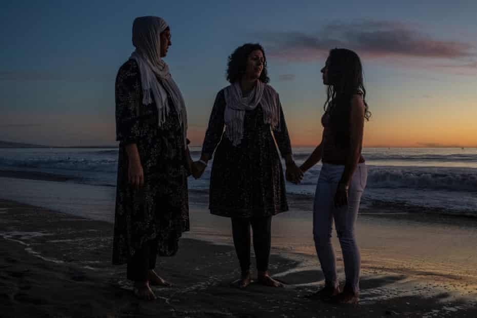 Trois femmes se tenant la main sur une plage au coucher du soleil
