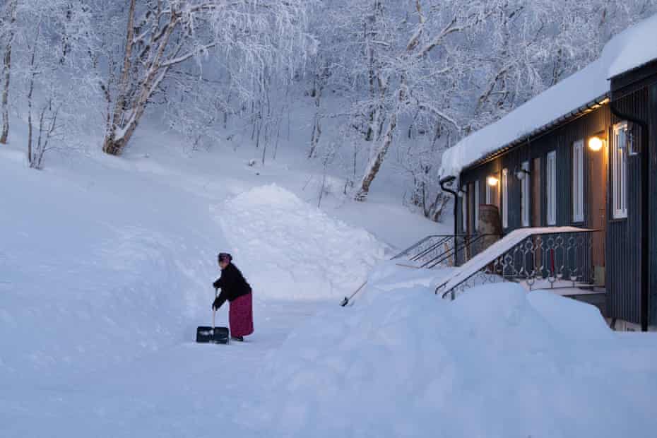 Une femme pellette de la neige à l'extérieur d'une cabane en bois