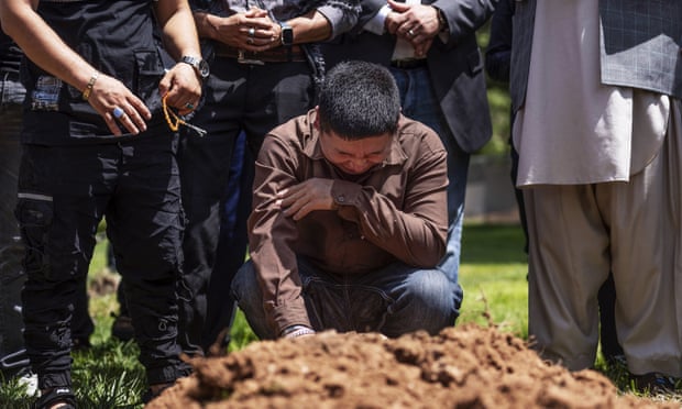 Un homme s'agenouille en pleurant dans un cimetière entouré d'autres personnes en deuil.